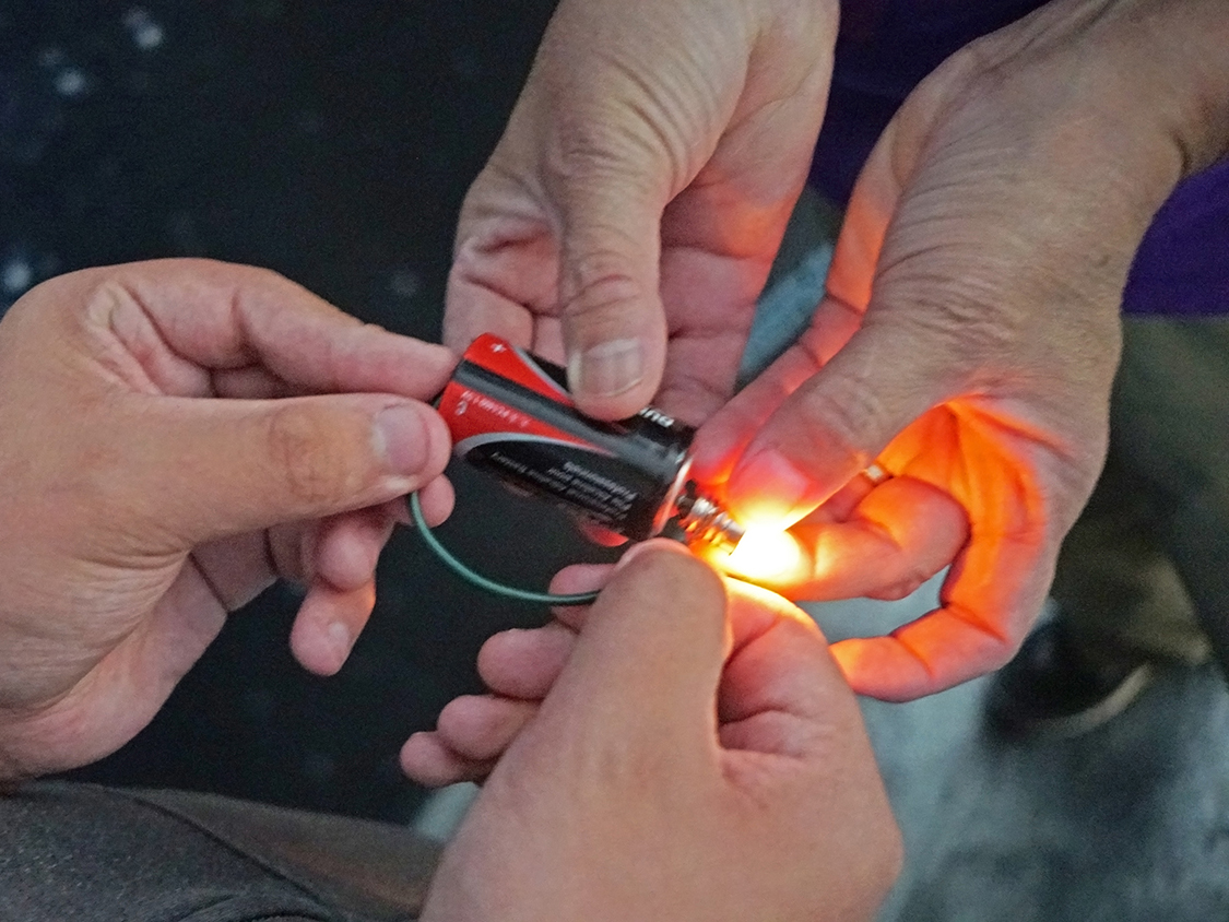 Using wires, student turn on a light bulb by connecting it to a battery